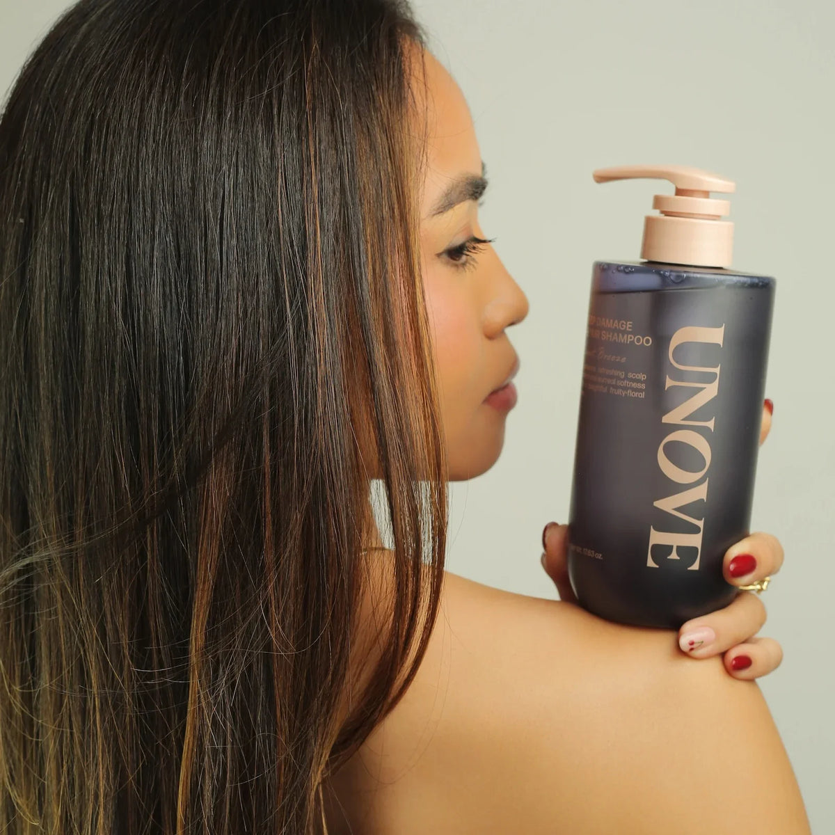 Woman holding UNOVE repair shampoo for damaged hair, showcasing sleek, healthy locks