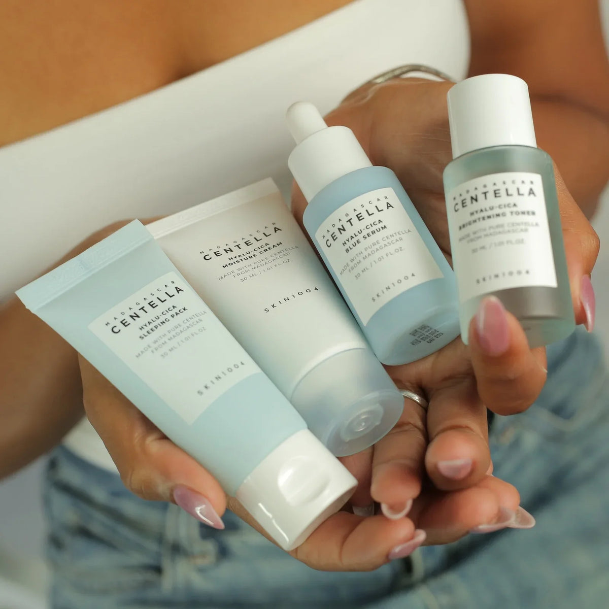 Hands holding Madagascar Centella skincare set: sleeping pack, moisture cream, blue serum, brightening toner