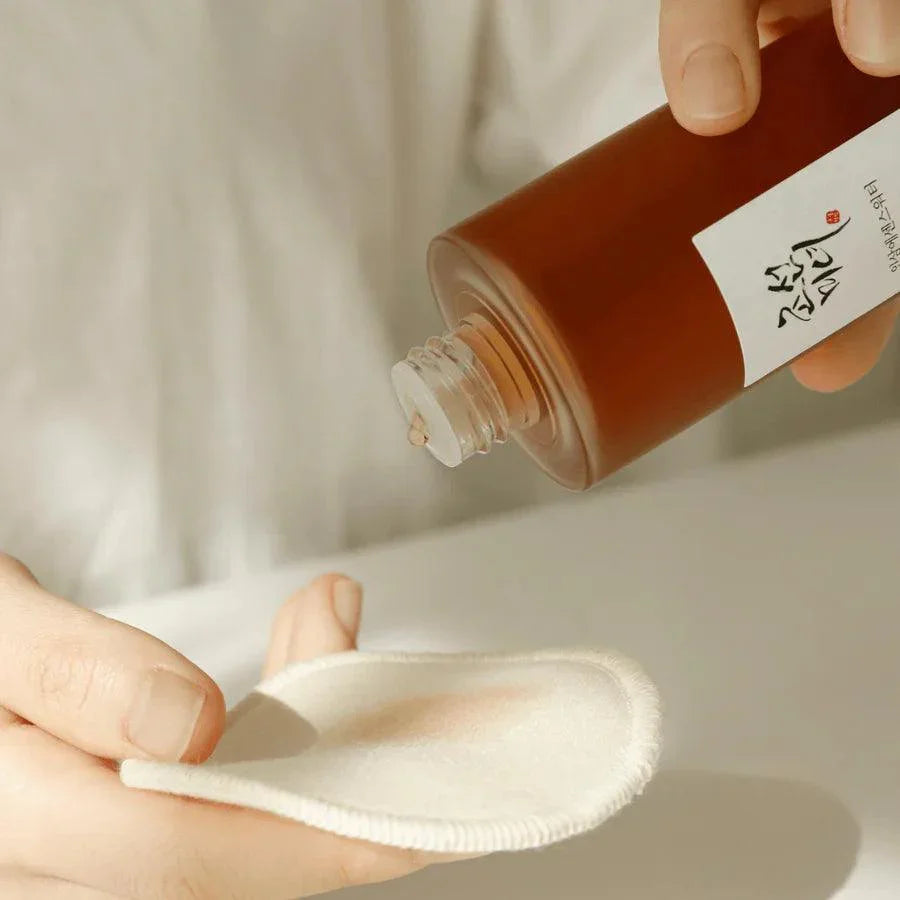 Hand pouring Korean skincare toner onto cotton pad for facial cleansing